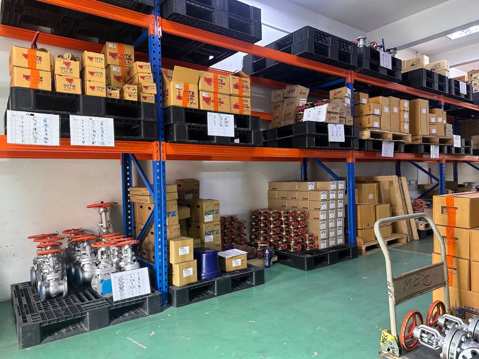 Warehouse racking holding cartons of valves and bronze stock, flanged gate valves laid out on pallets below