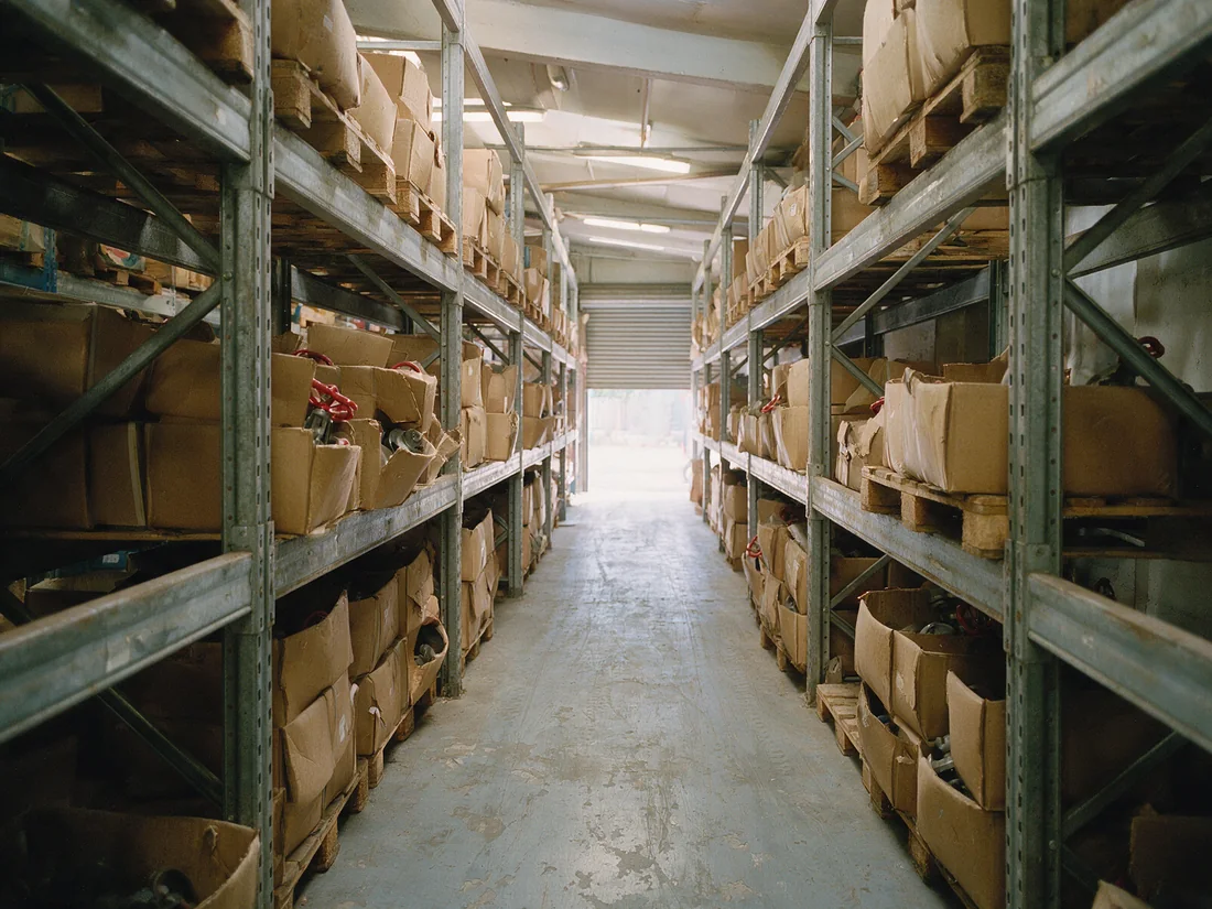 An aisle between warehouse racking runs, cartons of valve stock along the beams